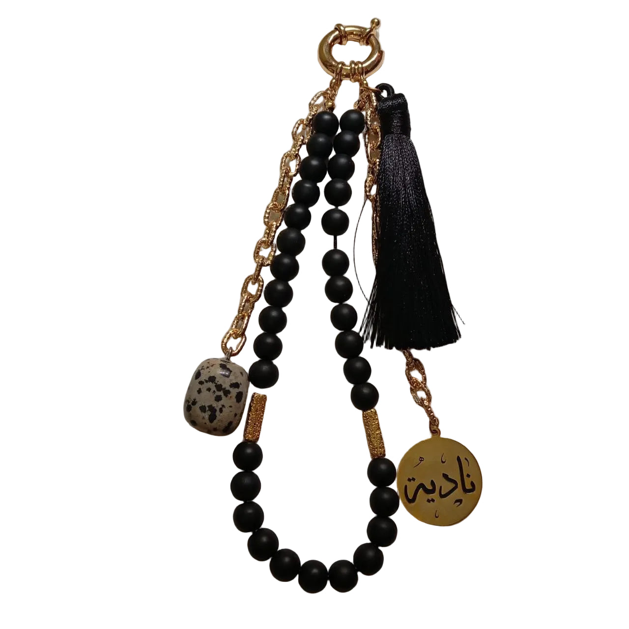 Black beaded keychain with gold accents and tassel on a textured white background