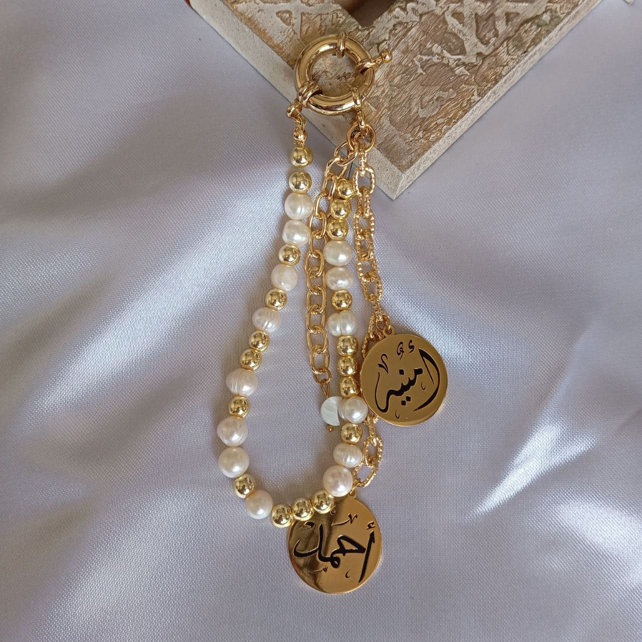 Gold chain with pearl beads and Arabic script charms on a white fabric background