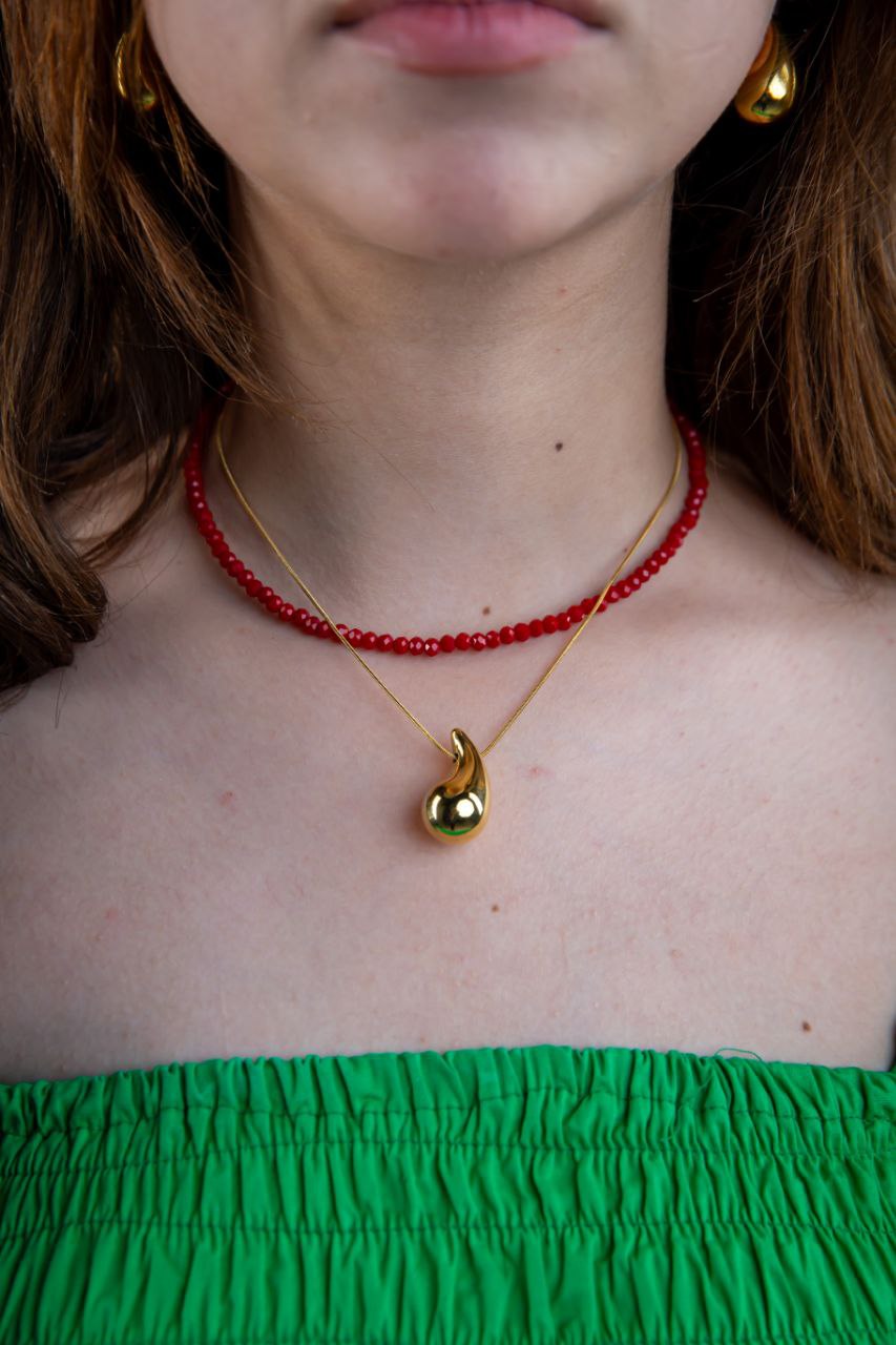 Person wearing a red beaded necklace and gold pendant necklace with a green top.