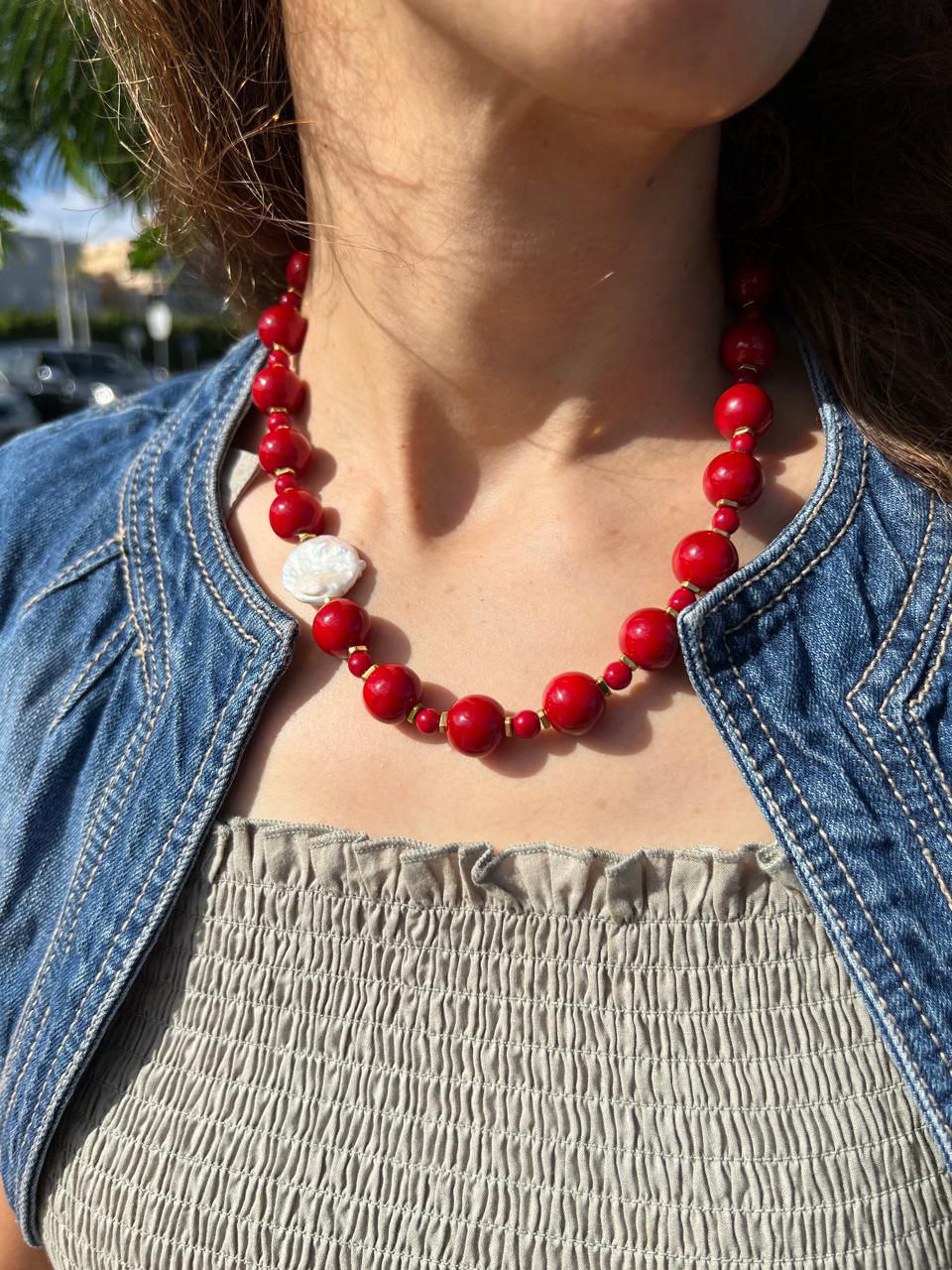 Person wearing a red beaded necklace with a denim jacket and beige top.