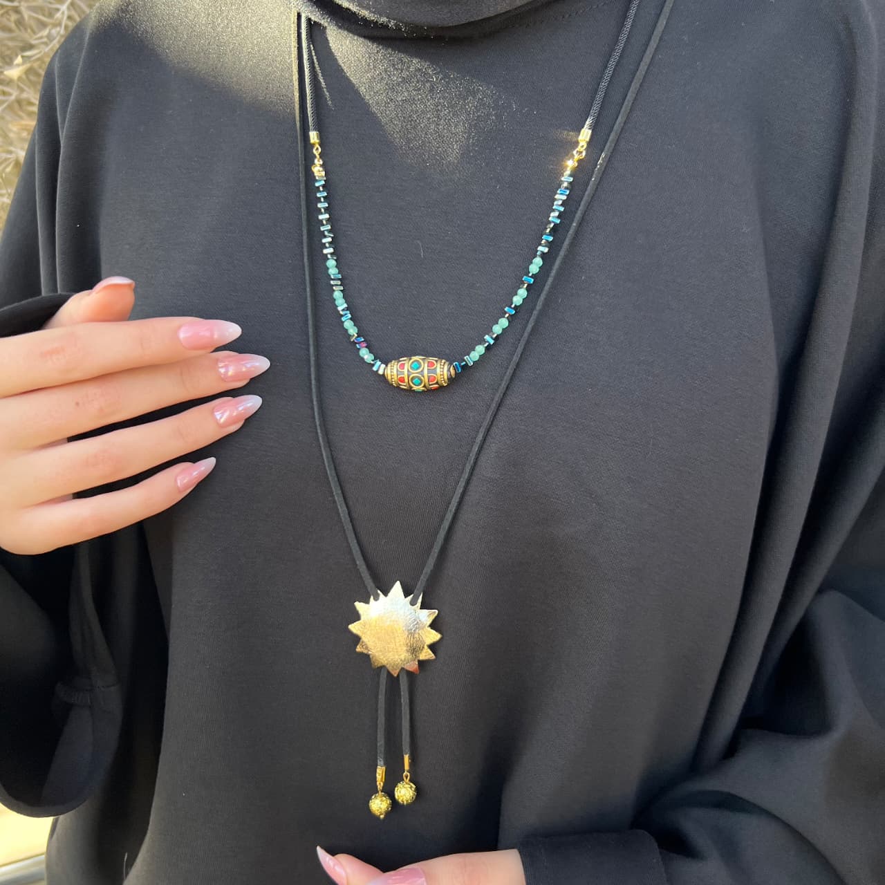 Necklace with a sun-shaped pendant worn by a person in a black outfit.