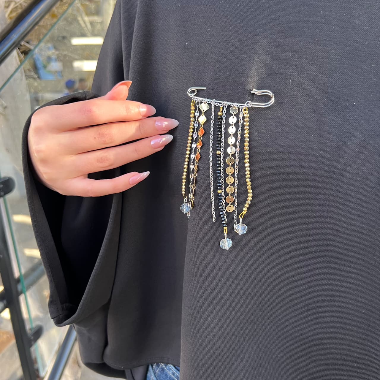 Hand holding a black garment with a jewelry hanger featuring necklaces against a dark background.