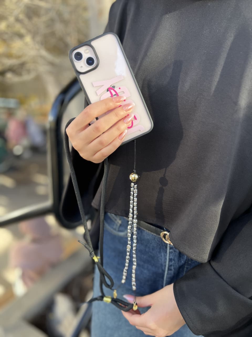 Person holding a phone with a case featuring a pink ribbon design, outdoors.