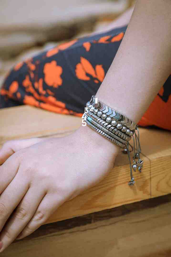 Close-up of a wrist with multiple silver bracelets on a wooden surface.