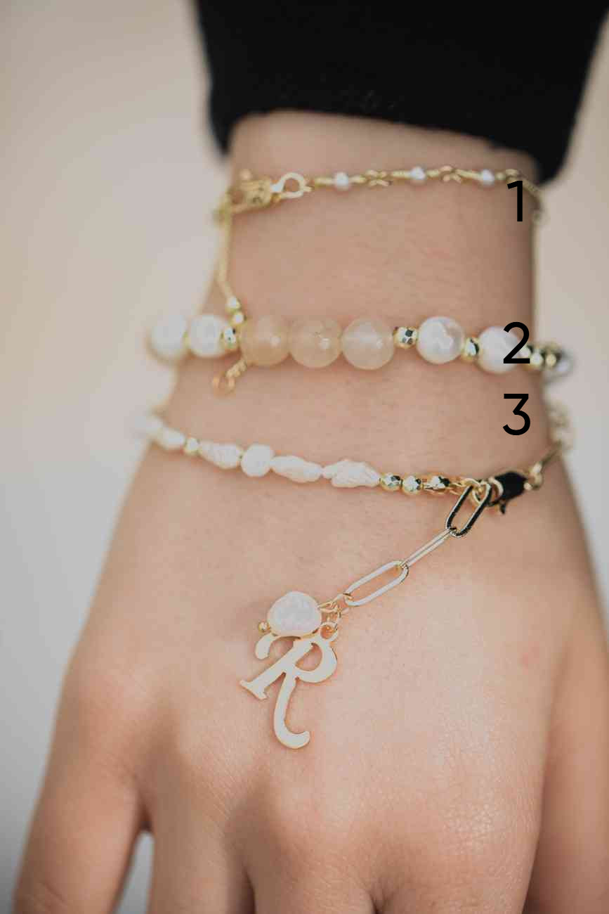 Three bracelets on a wrist with visible charms against a neutral background