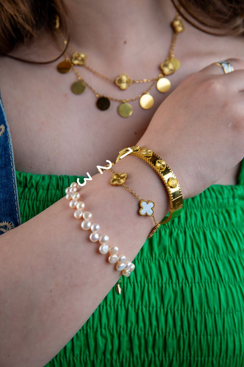 Close-up of a person's wrist wearing gold bracelets and a pearl bracelet against a green fabric background.