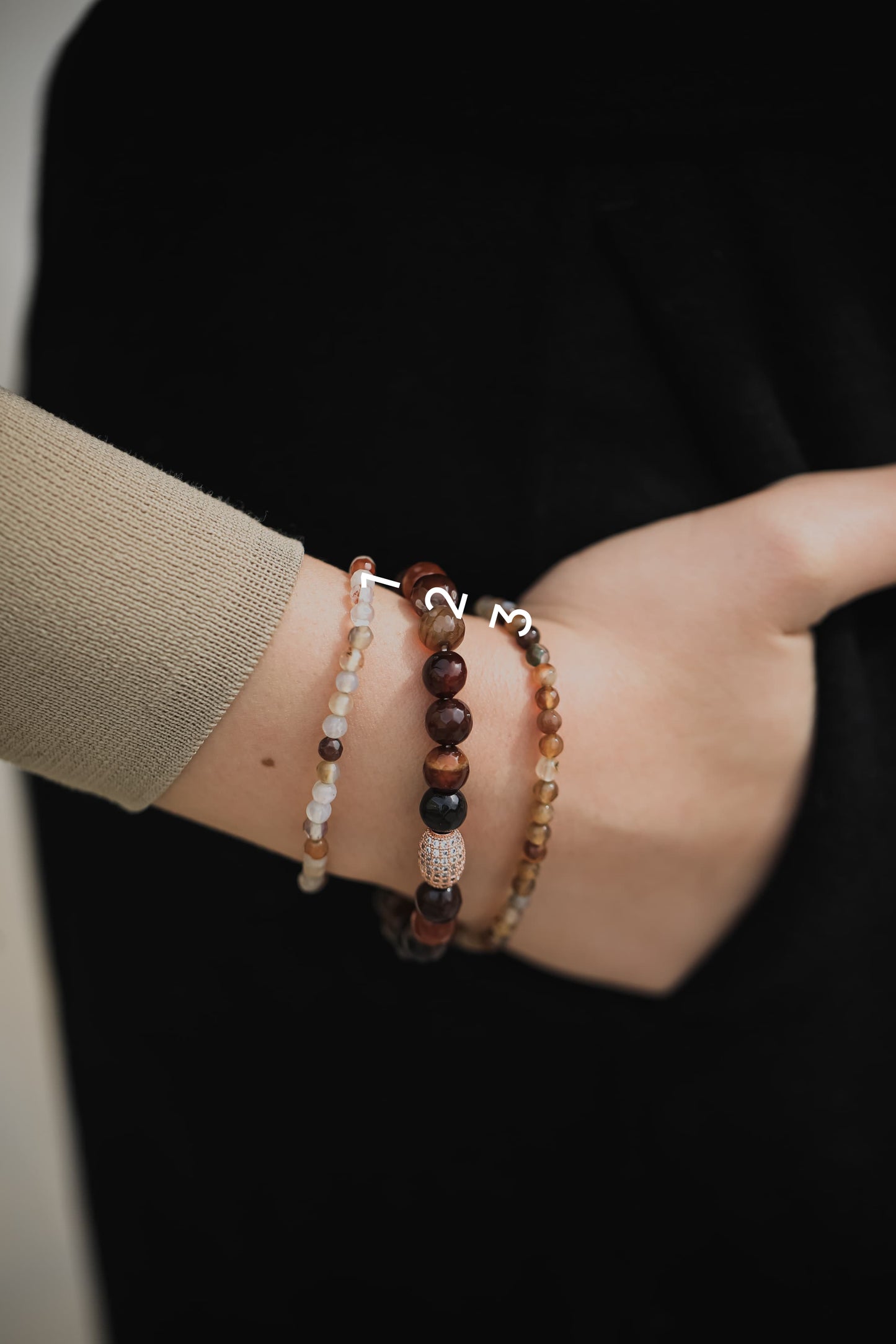 Hand wearing multiple beaded bracelets on a dark background