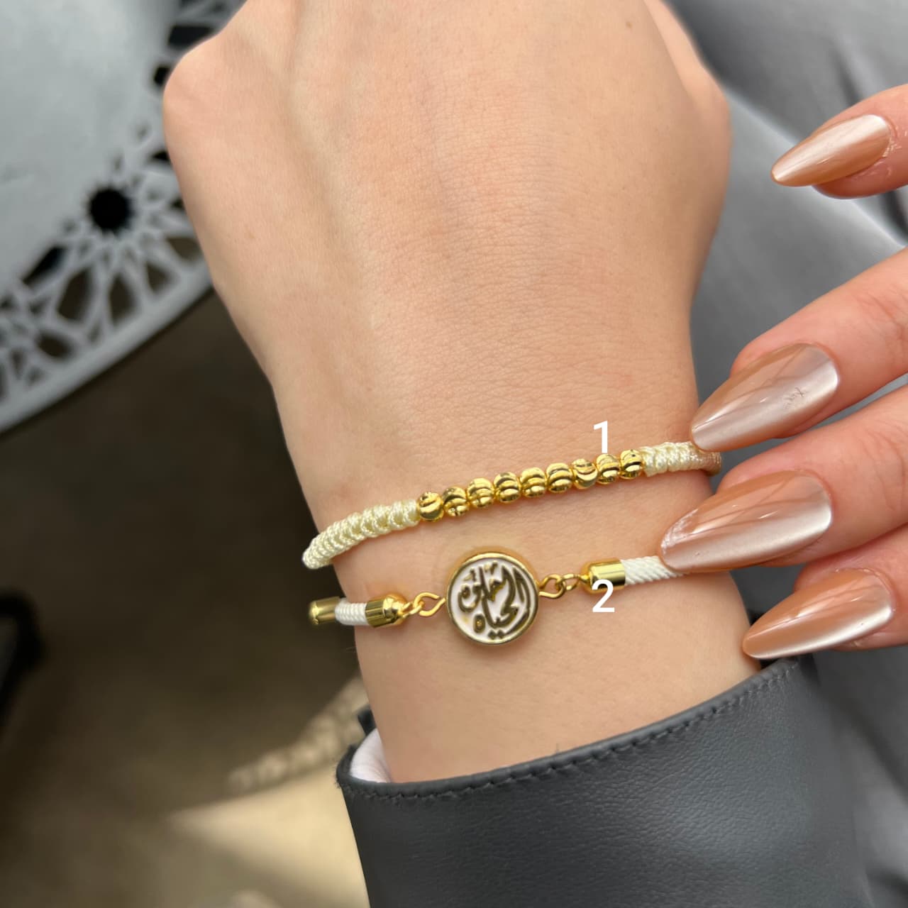 Gold bracelet with a circular charm on a wrist against a neutral background