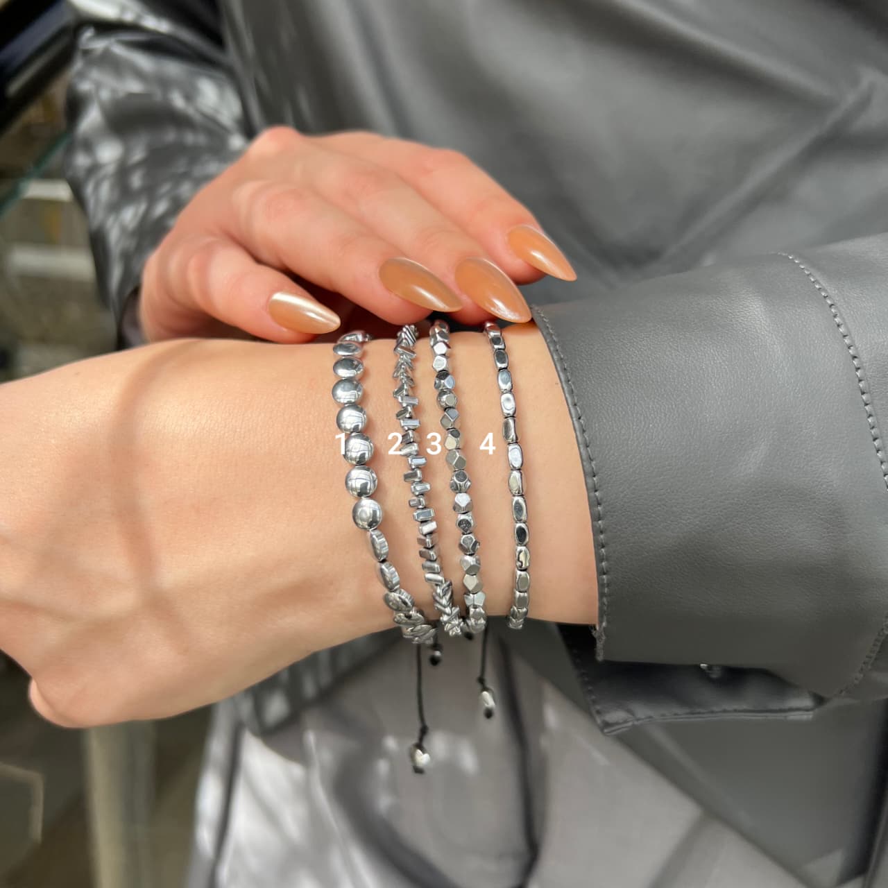 Close-up of a wrist wearing multiple silver beaded bracelets with a blurred background