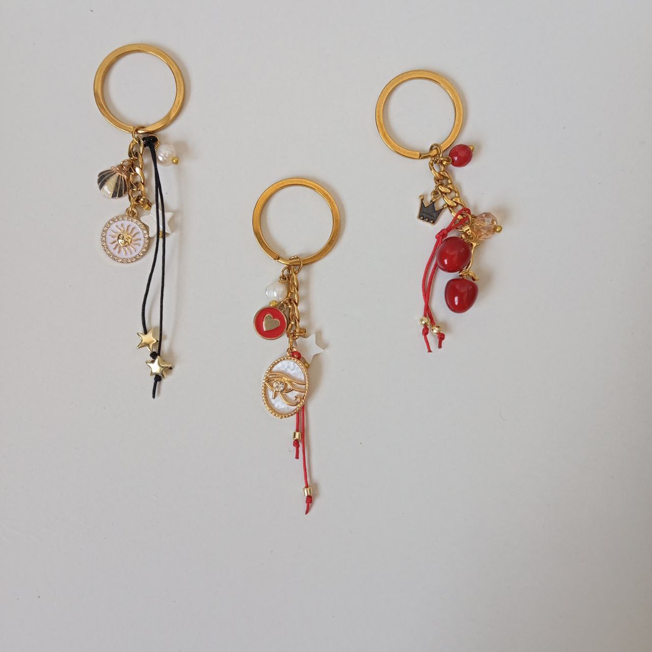  handmade key and bag chains with gold rings, red and pink beaded charms, and elegant metallic details on a neutral background."