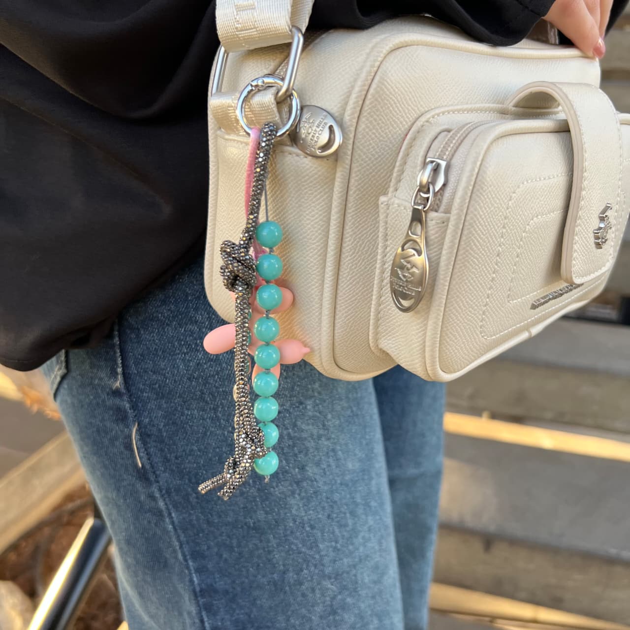 Beige handbag with turquoise charm held by a person wearing jeans.