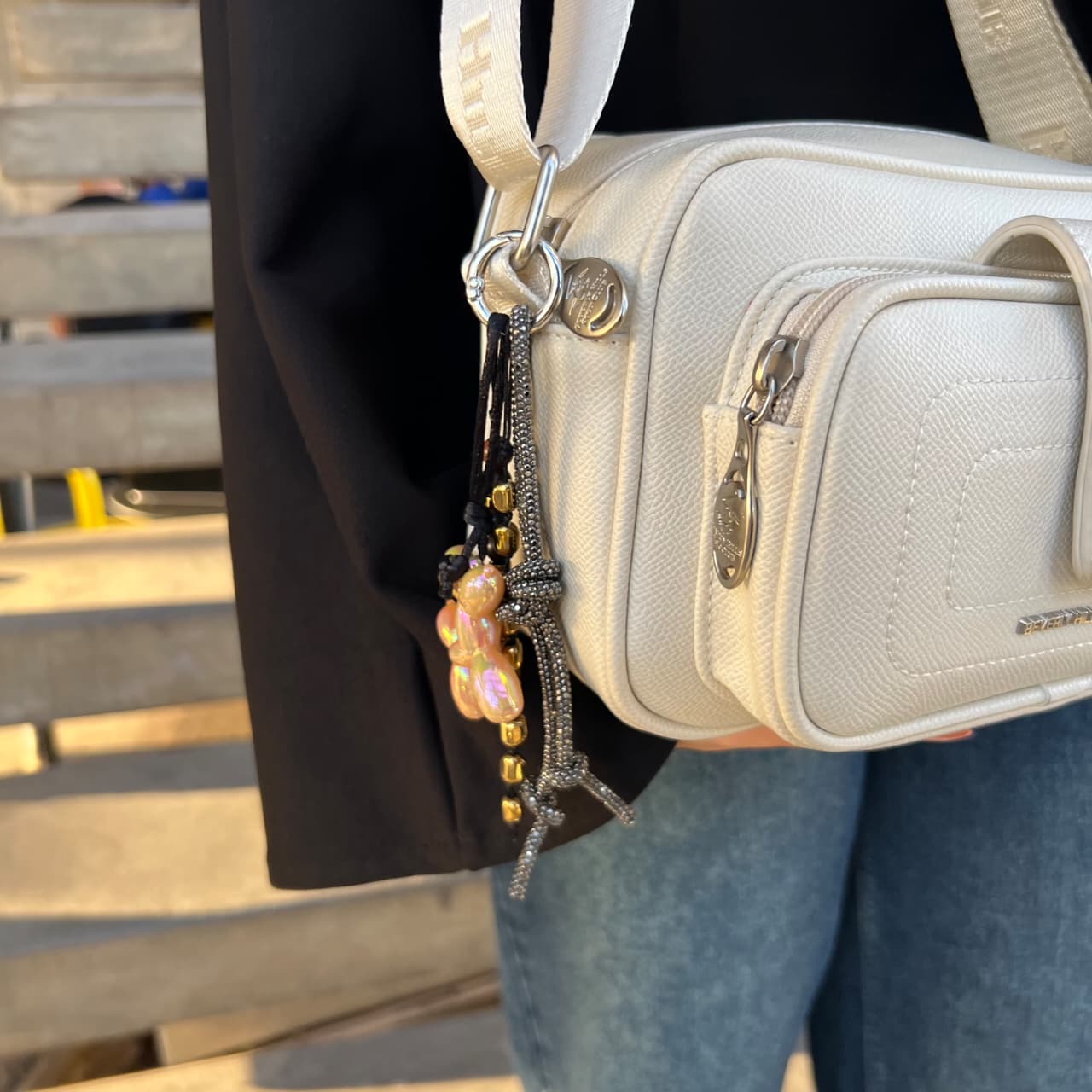White handbag with a decorative charm worn by a person sitting on a bench.