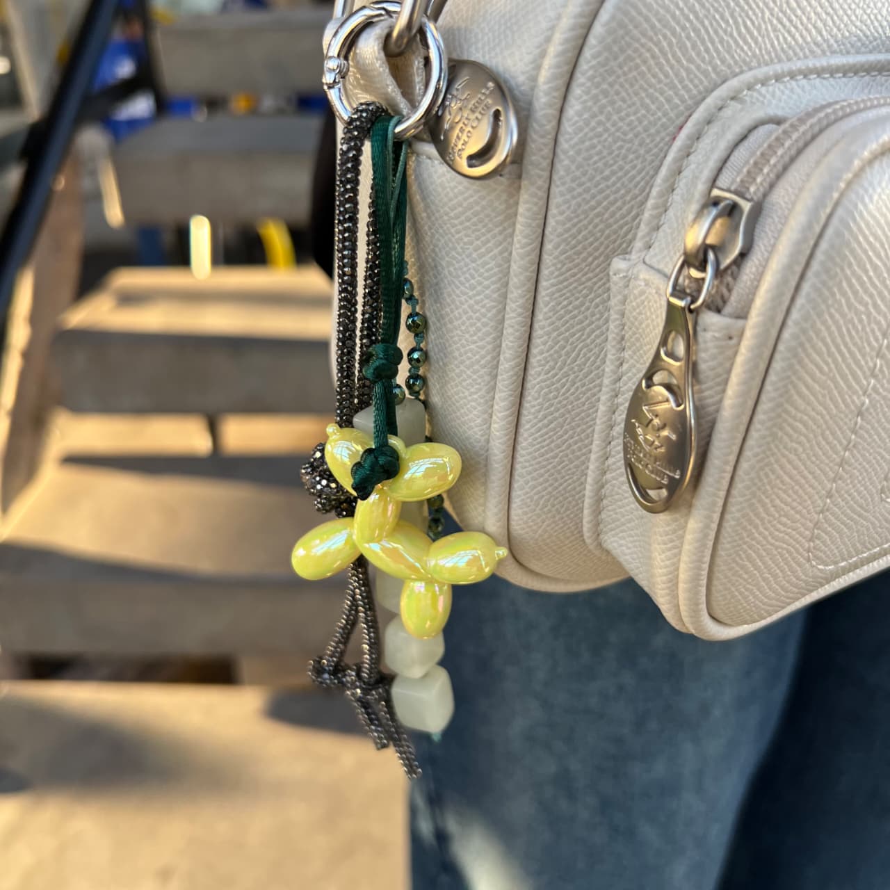 Close-up of a beige handbag with a decorative keychain featuring yellow flowers and green leaves.