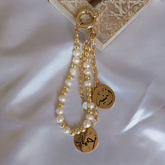 Gold chain with pearl beads and Arabic script charms on a white fabric background