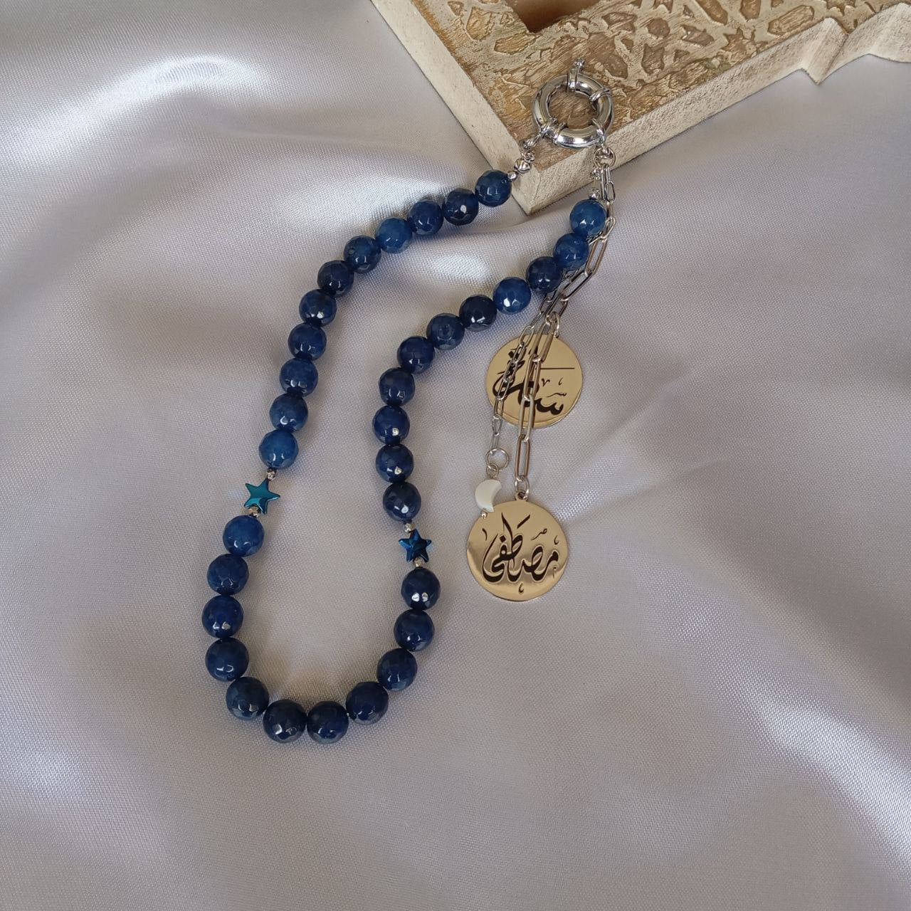 Blue beaded necklace with gold charms on a satin surface