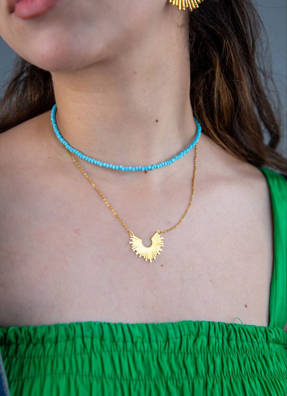 Close-up of a person wearing a gold necklace with a unique pendant and a turquoise beaded choker.