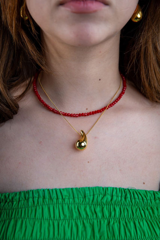 Person wearing a red beaded necklace and gold pendant necklace with a green top.