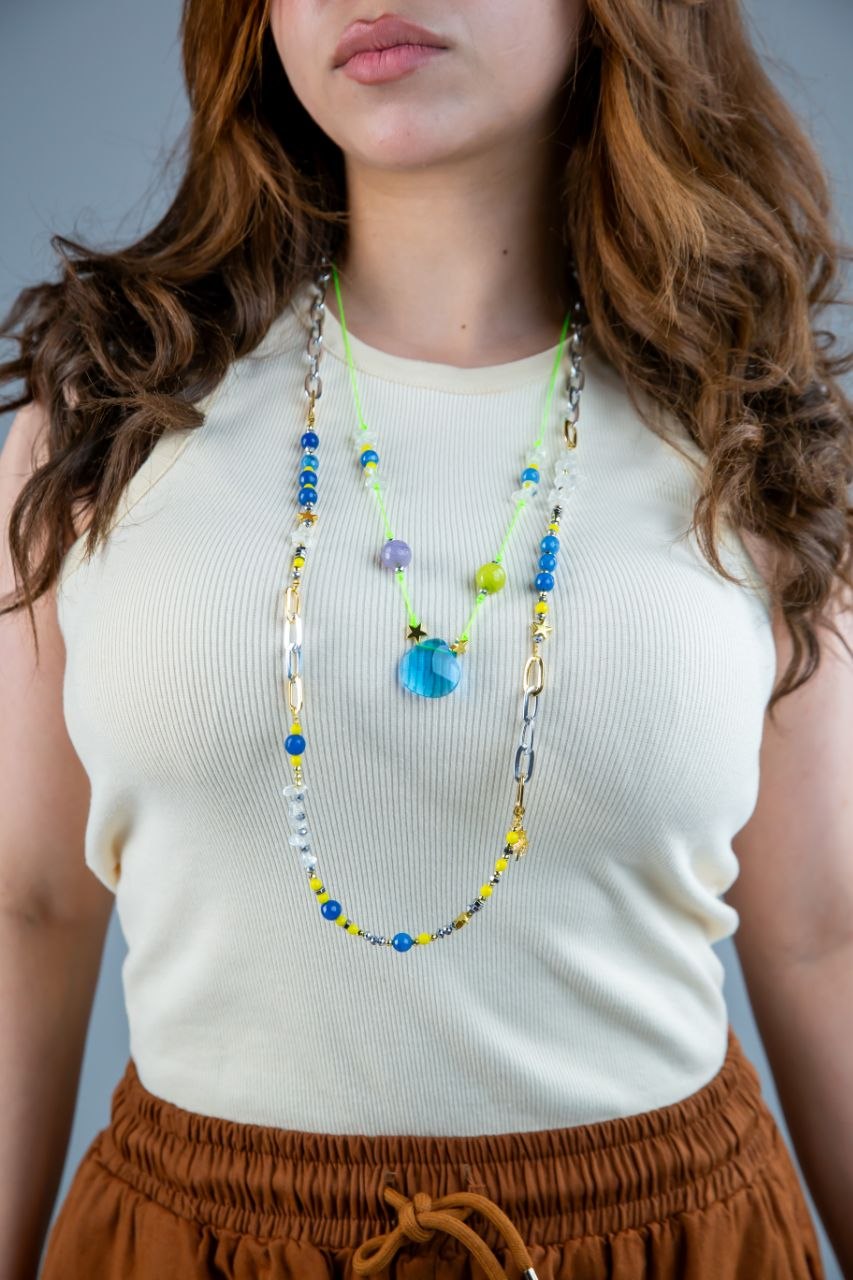Person wearing a white sleeveless top and brown pants with a colorful beaded necklace.