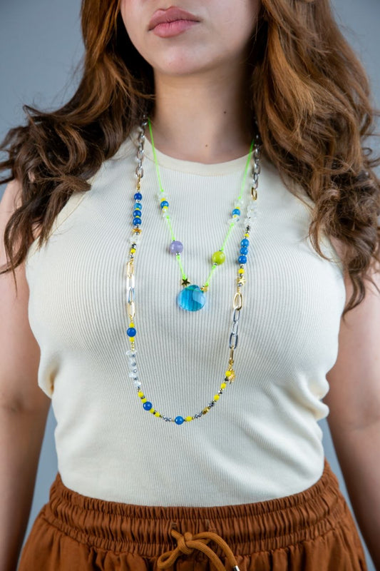 Person wearing a white sleeveless top and brown pants with a colorful beaded necklace.