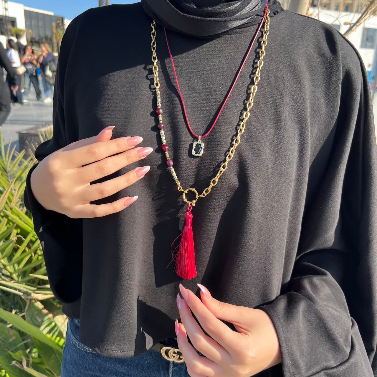 Person wearing a black outfit with a long necklace featuring a red tassel.