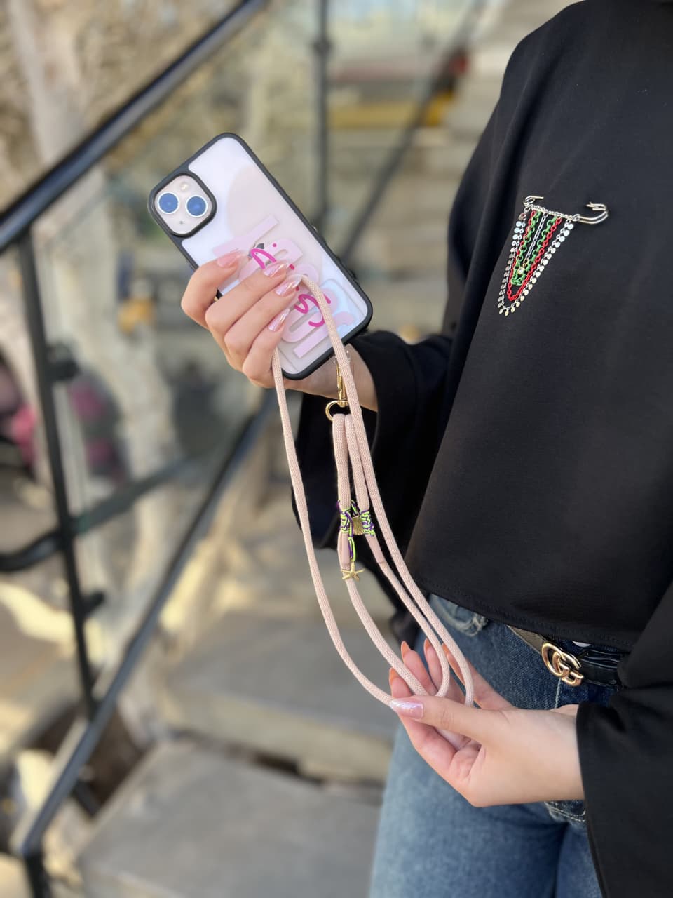 Person holding a phone with a pink case and strap, standing on a staircase.