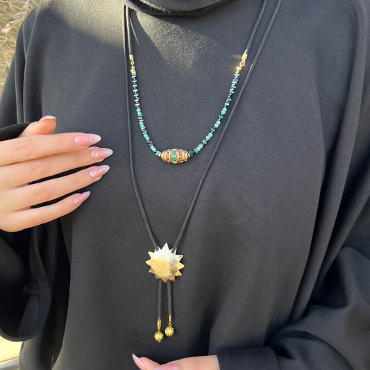 Necklace with a sun-shaped pendant worn by a person in a black outfit.