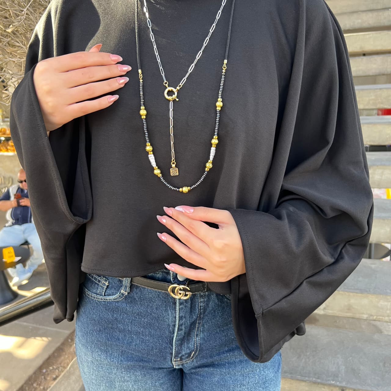 Person wearing a black sweater and blue jeans with layered necklaces.