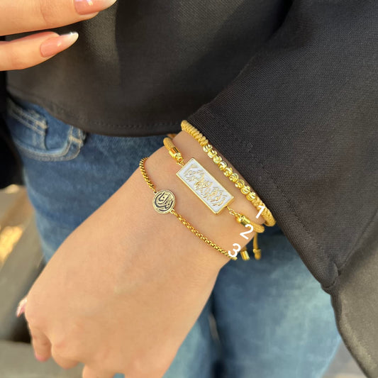 Gold bracelets on a person's wrist with a black sleeve and blue jeans.