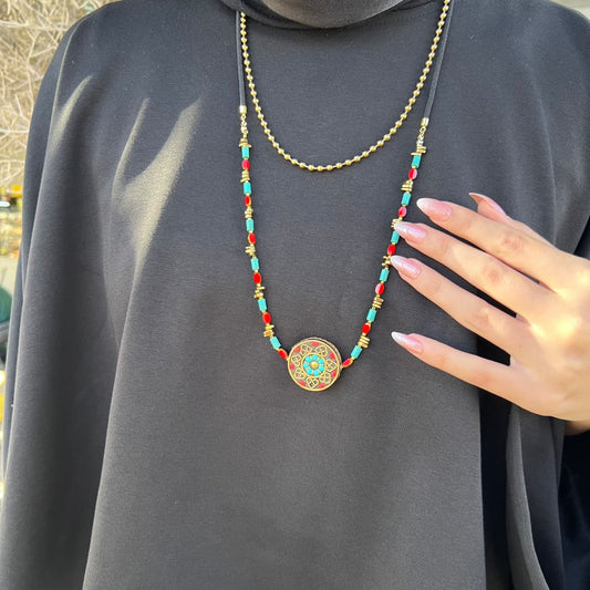 Colorful beaded necklace with a decorative pendant on a person wearing a dark gray outfit.