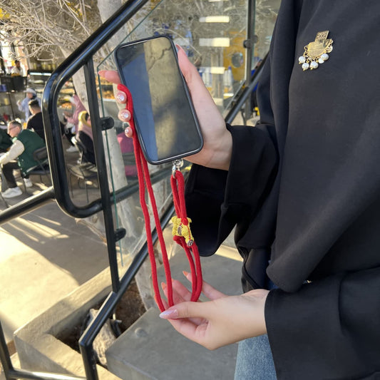 Person holding a phone with a red strap, wearing a black coat with a brooch.
