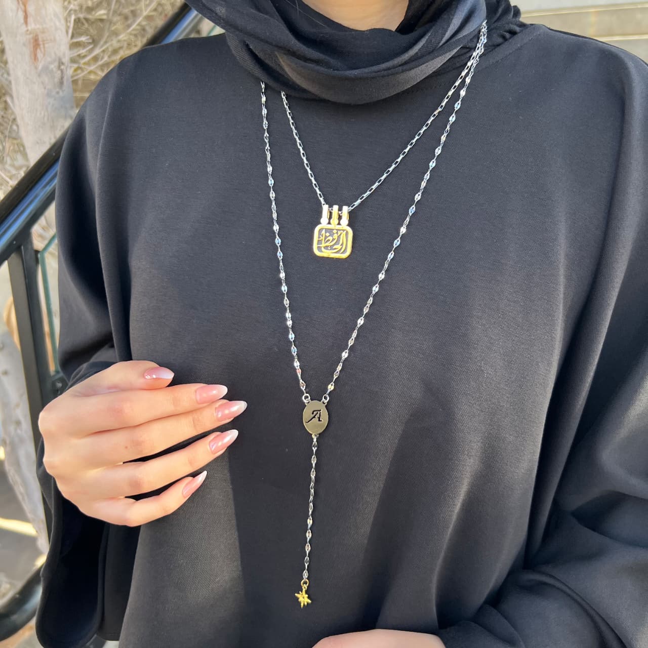 Person wearing a dark gray outfit with layered necklaces featuring various pendants.