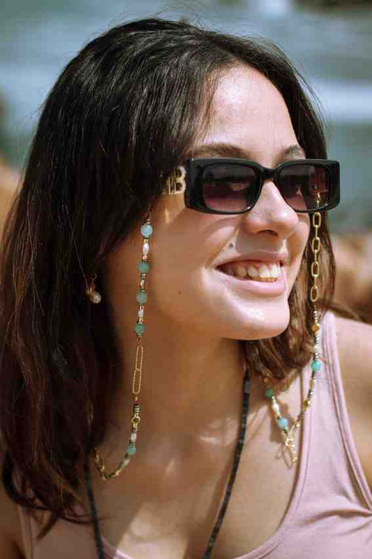 A person wearing sunglasses and a necklace with gold-colored chains and what appears to be amber stones.