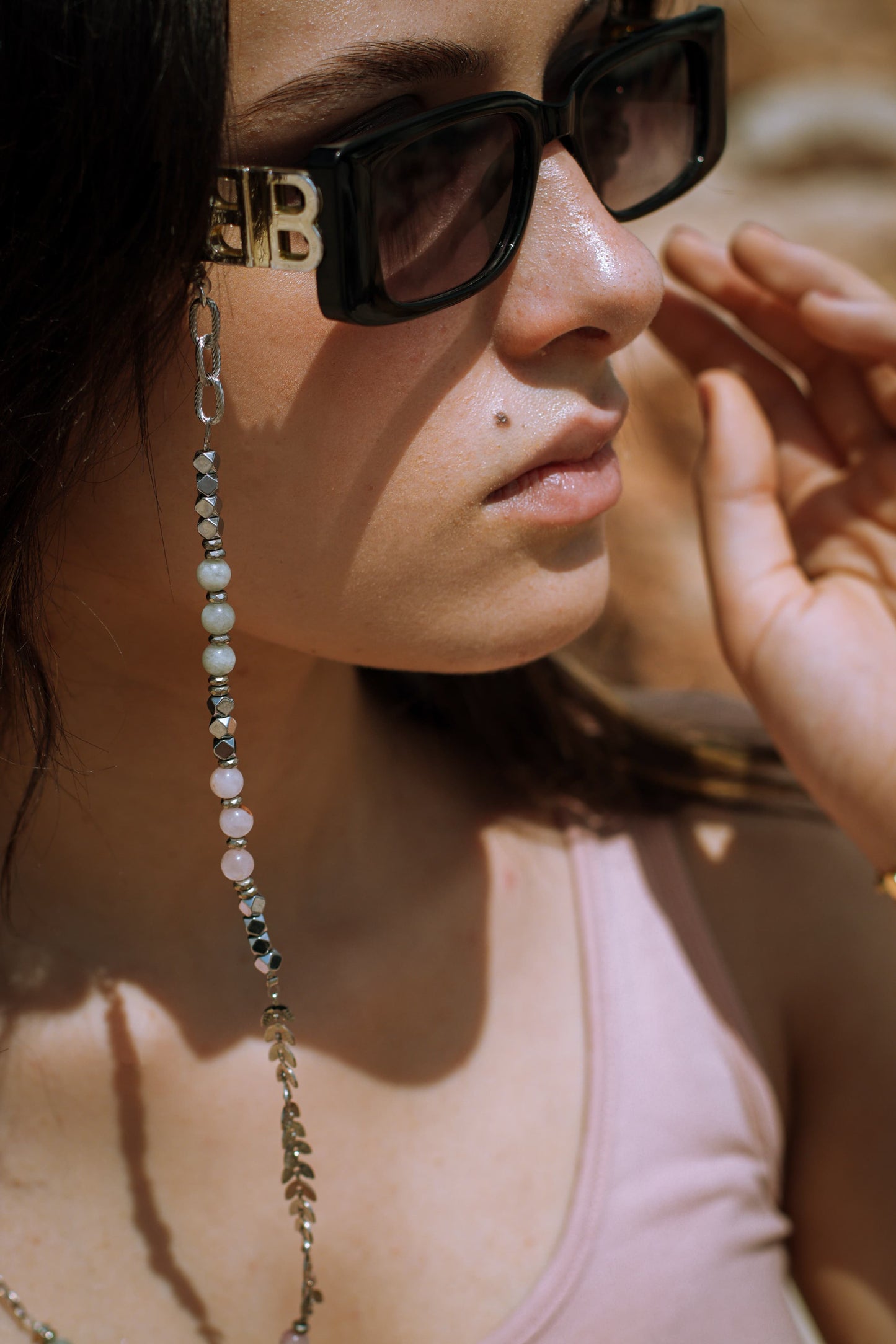 Close-up of a person wearing sunglasses with a chain detail, outdoors.