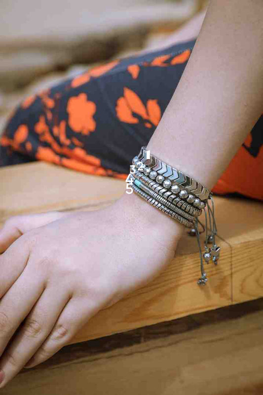 Close-up of a wrist with multiple silver bracelets on a wooden surface.