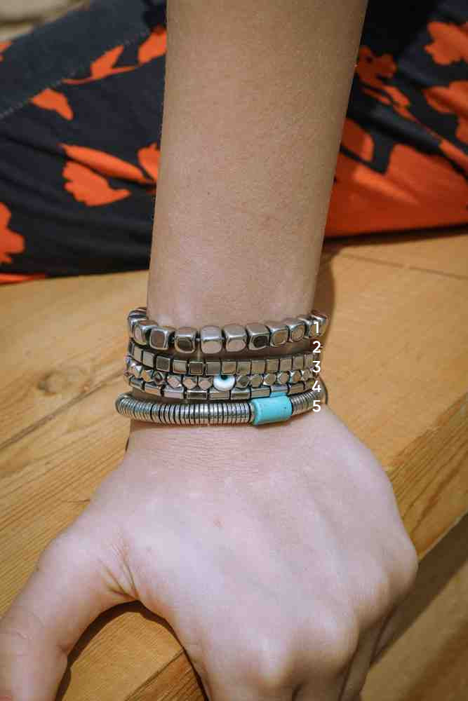 Close-up of a wrist wearing multiple bracelets on a wooden surface.