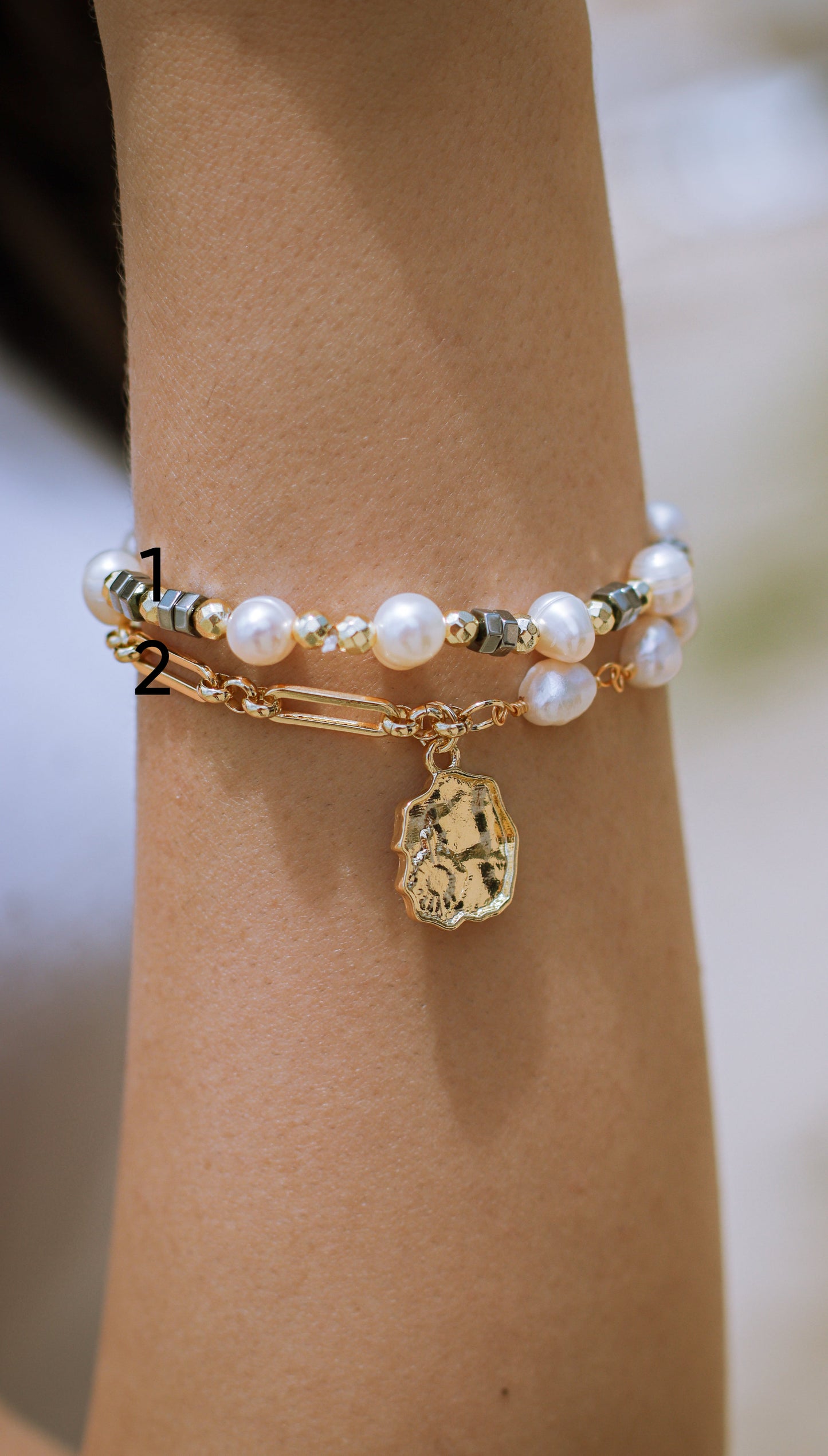 Gold bracelet with pearls and a charm on a wrist against a neutral background