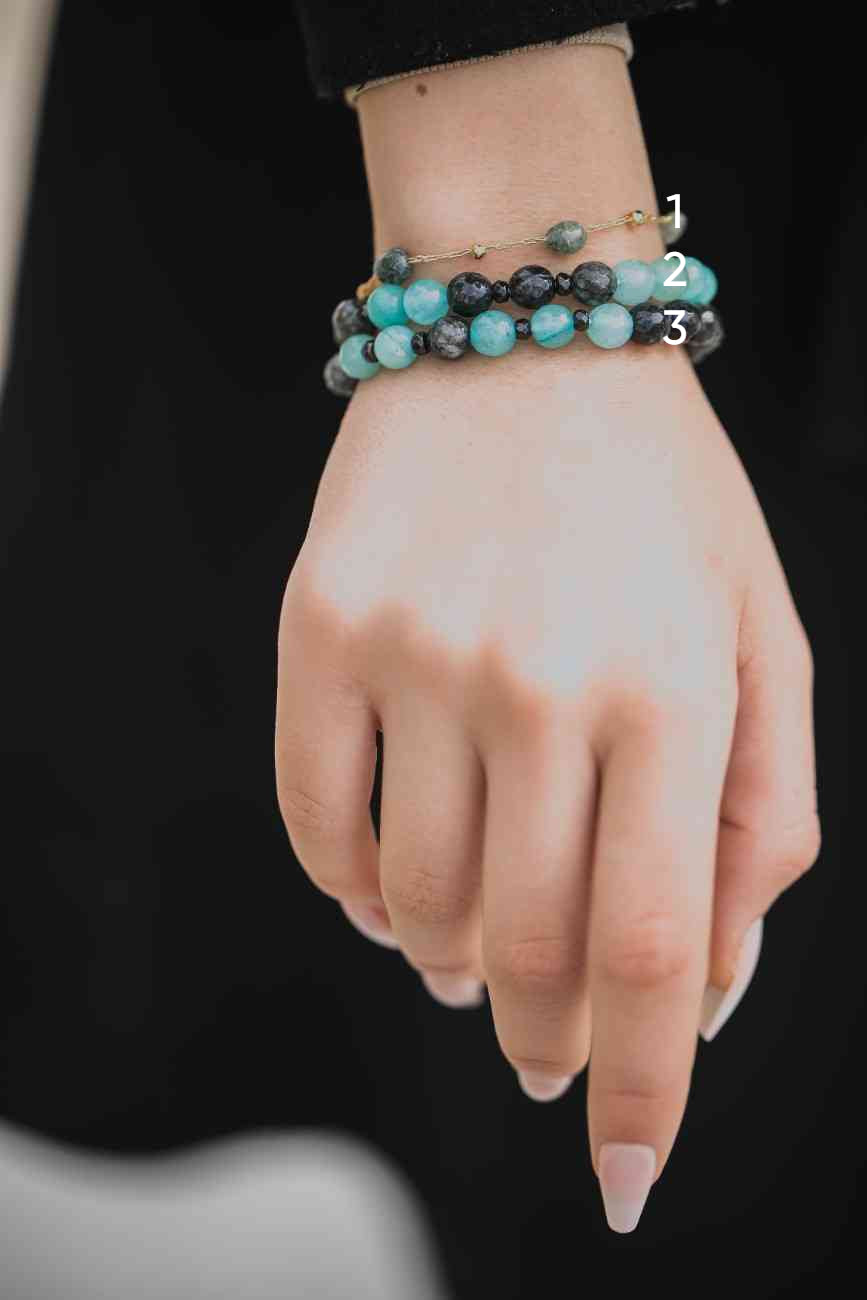Hand wearing three turquoise beaded bracelets on a black background