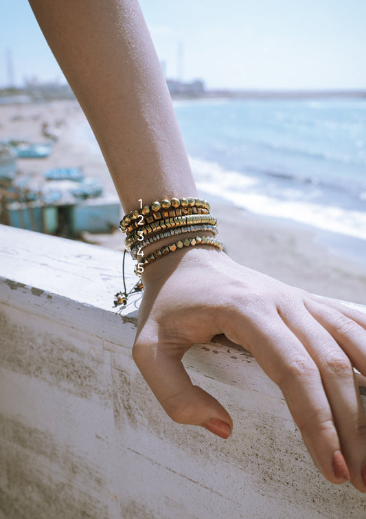 Hand wearing gold bracelets with a blurred coastal background