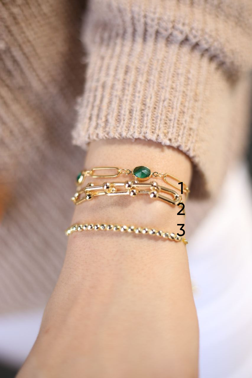 Gold bracelets with green gemstone on a wrist against a neutral background