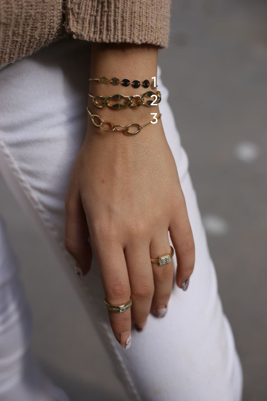 Hand wearing gold bracelets and rings with a blurred background