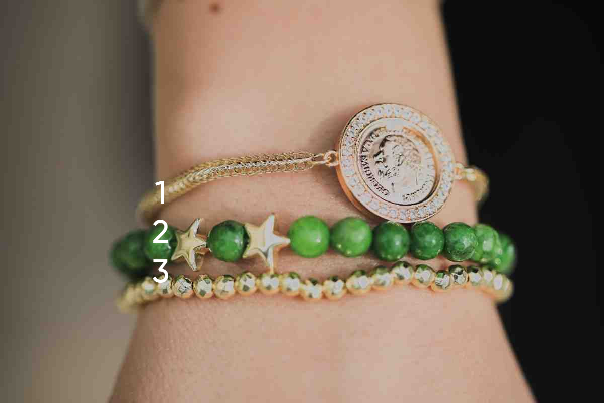 Close-up of a wrist wearing multiple bracelets with green beads and gold accents.
