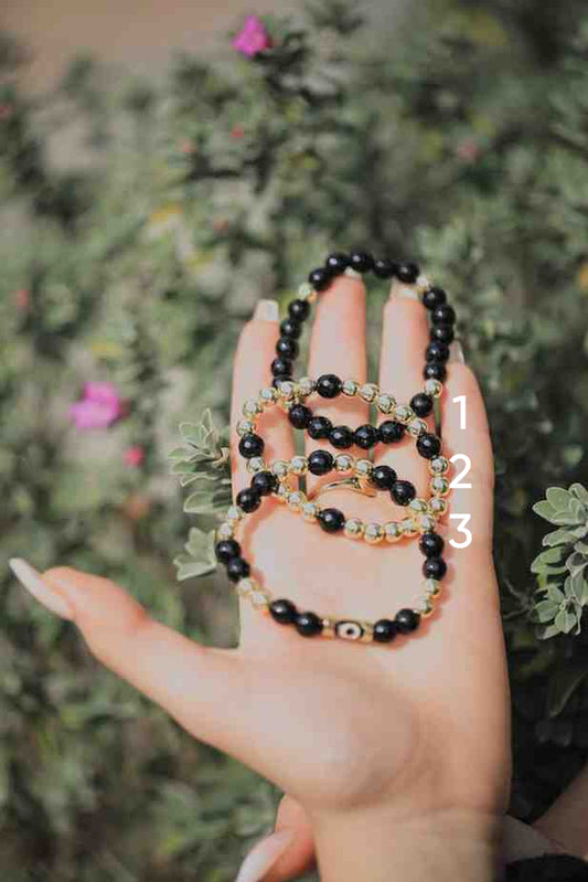 Hand holding three black beaded bracelets with a blurred green background