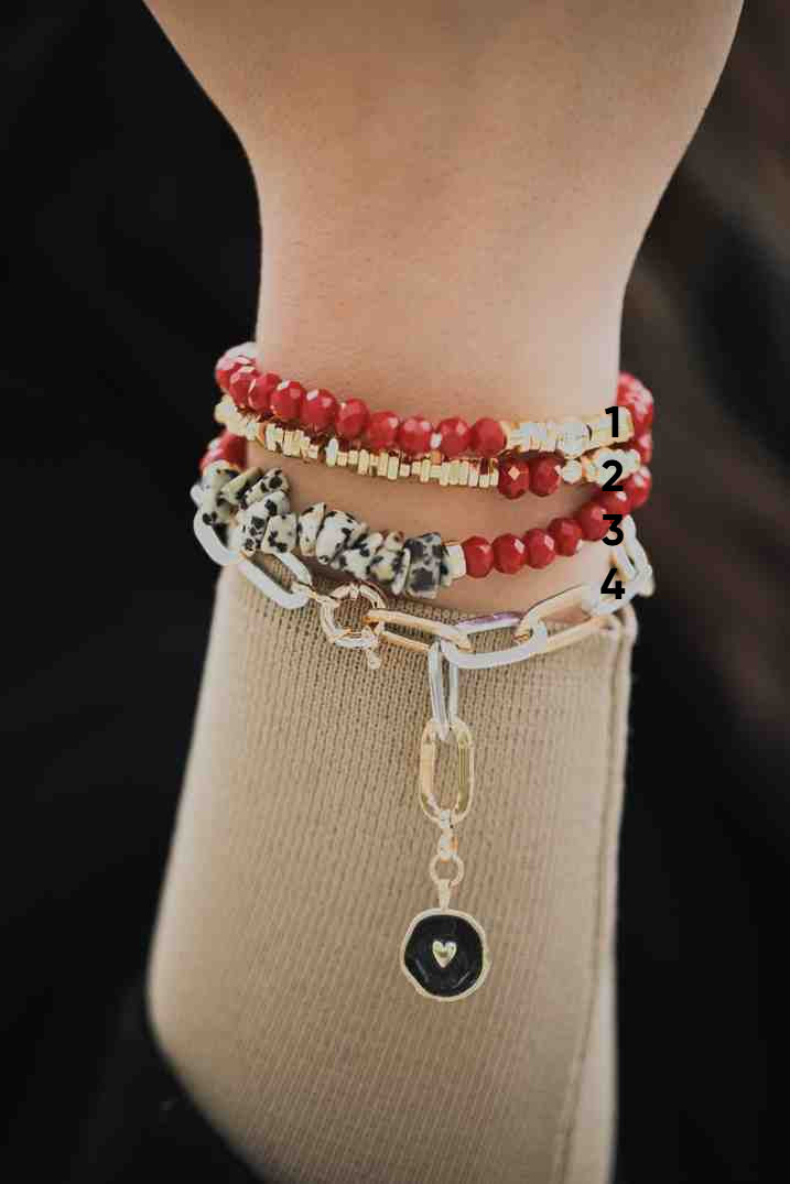 Close-up of a wrist wearing multiple bracelets with beads and charms on a dark background