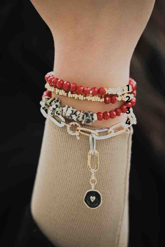 Close-up of a wrist wearing multiple bracelets with beads and charms on a dark background