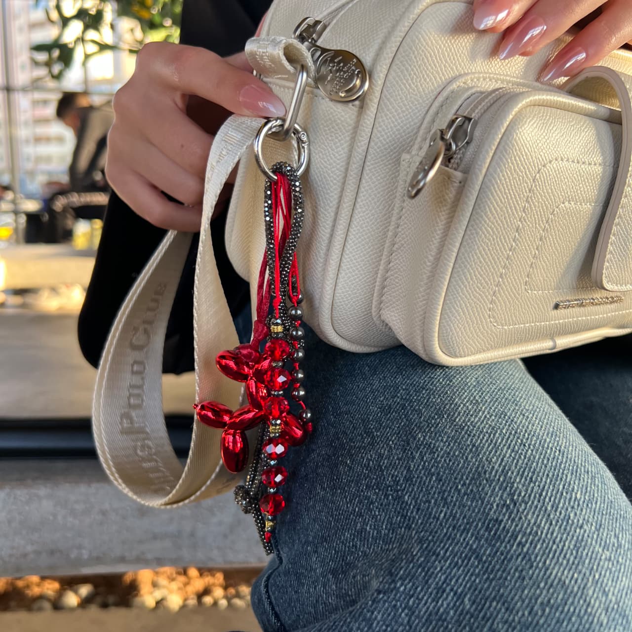 Beige handbag with a red and black beaded strap held by a person.