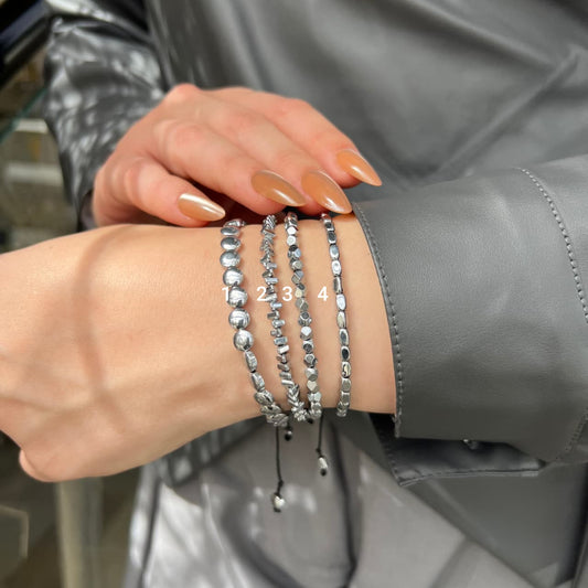 Close-up of a wrist wearing multiple silver beaded bracelets with a blurred background